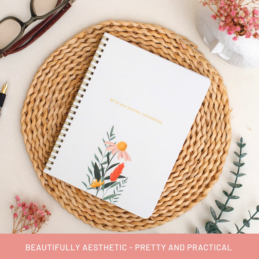 Flat lay of Happy Hoos “Joyful Journey” aesthetic summer spiral notebook with gold coil, white floral cover, and the quote “Write your journey, cultivate joy,” shown with the text “Beautifully aesthetic – pretty and practical” — perfect for gratitude journaling, daily planning, and summer gift ideas.