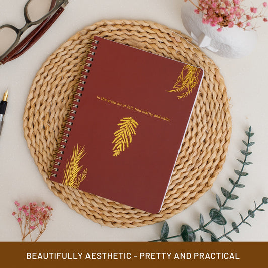Maroon notebook with gold leaf design on a woven mat with decorative elements.