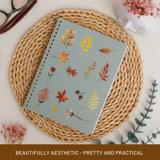 Notebook with autumn leaf design on a woven mat with decorative elements.