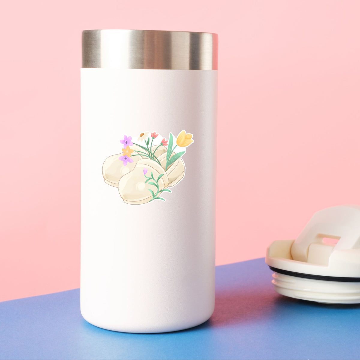 White tumbler with floral design on a pink and blue background