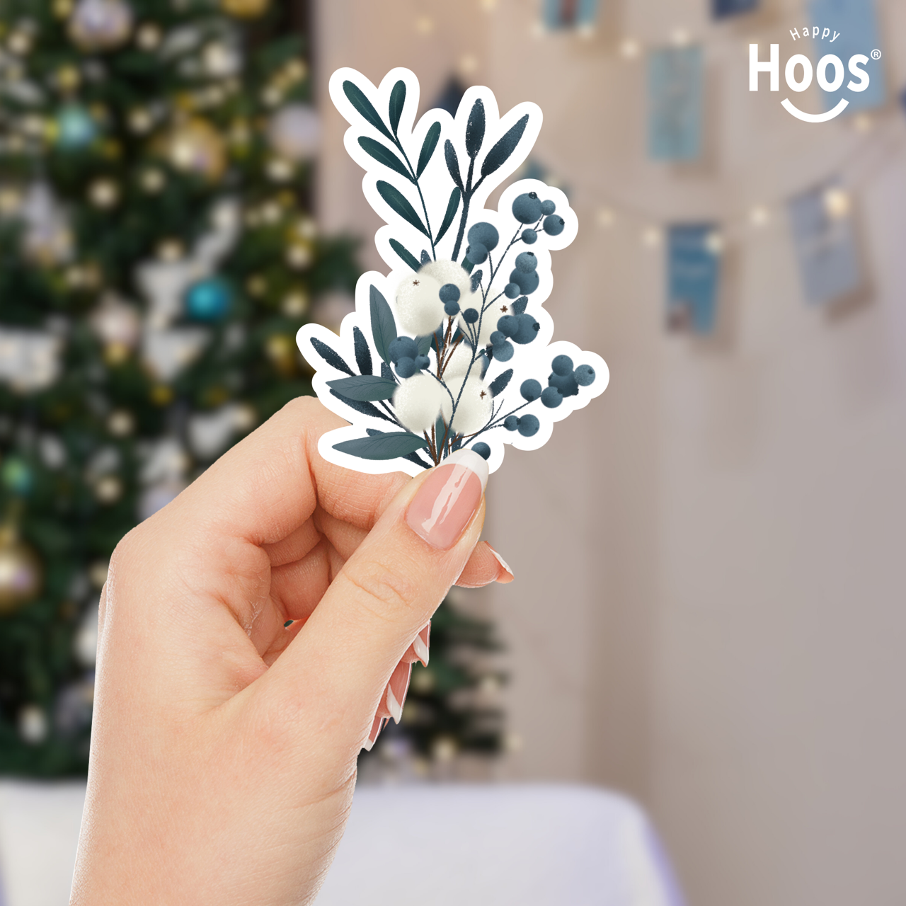 Hand holding a Winter Eucalyptus floral sticker with a blurred Christmas tree in the background