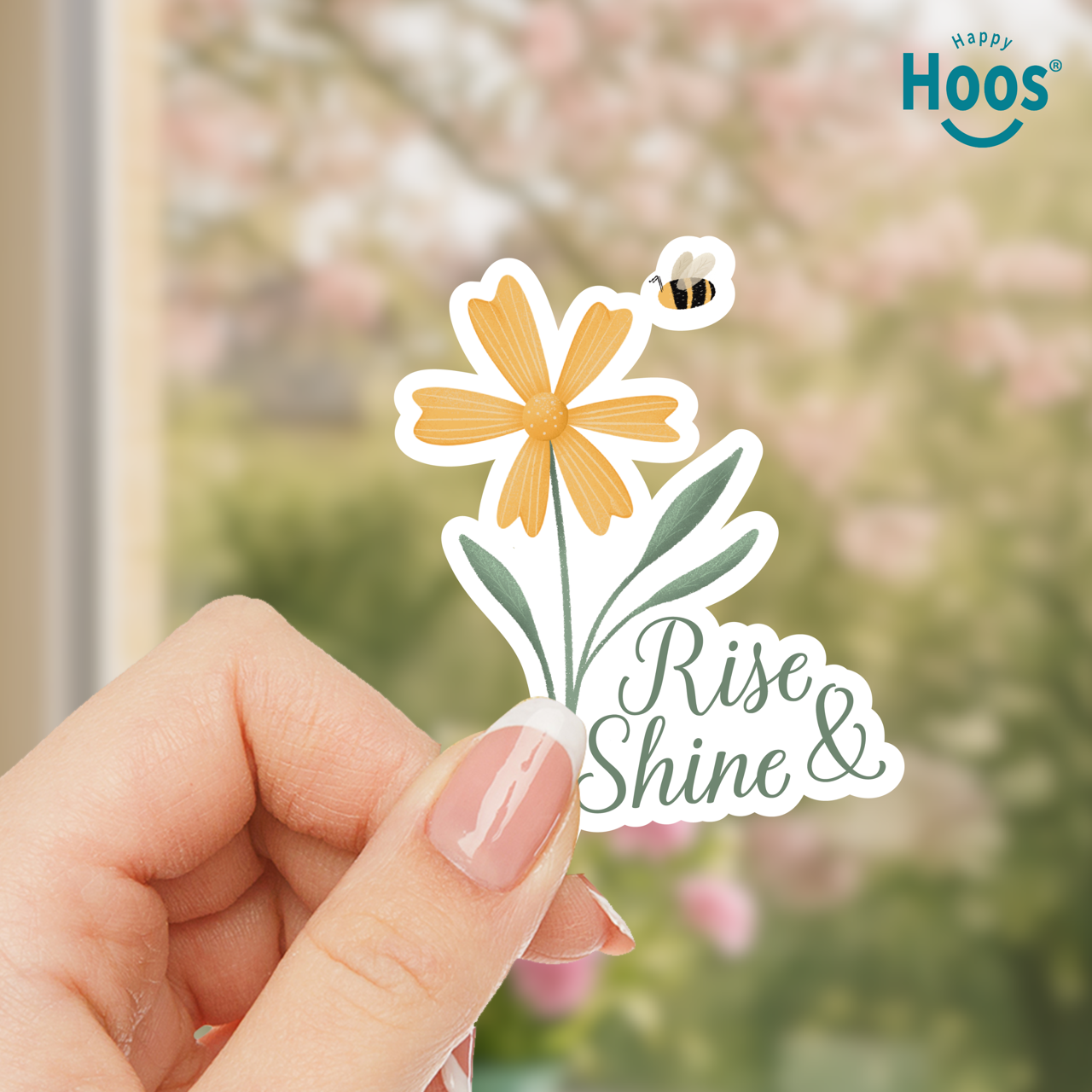 Hand holding a sticker with a flower and bee design and 'Happy Hoos' branding.
