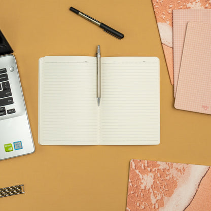 Open notebook with a pen on a brown surface with stationery items around