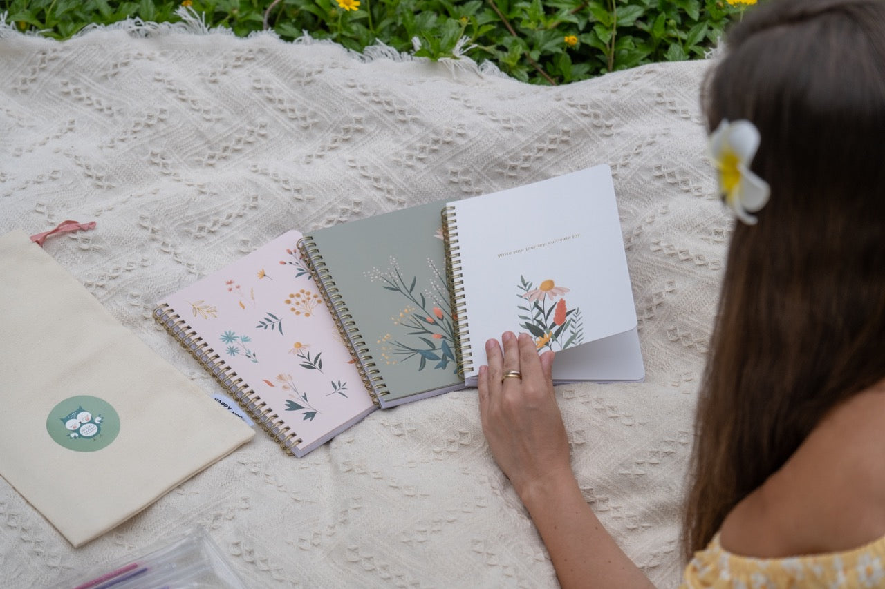 Person sitting on a textured blanket outdoors with floral notebooks