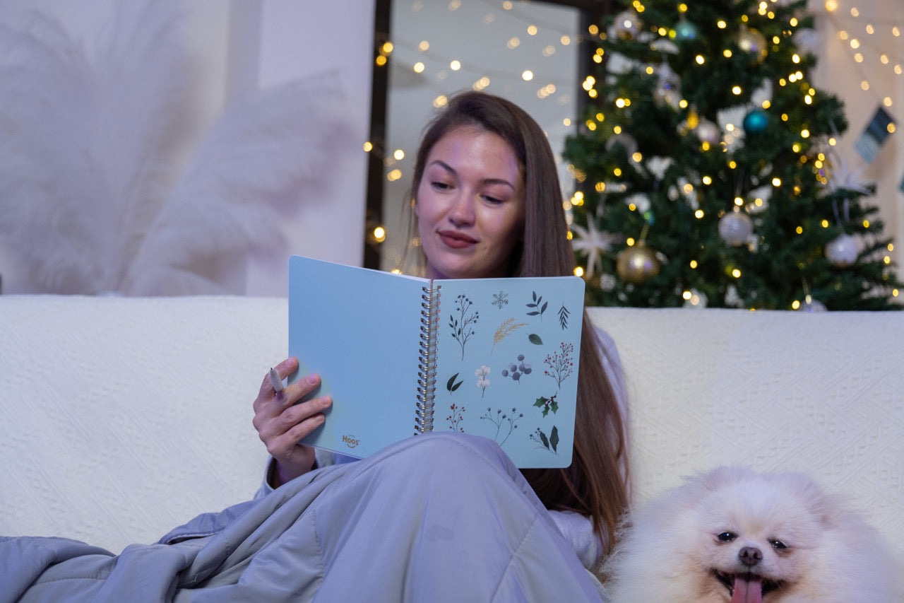 Woman reading a book with a dog sitting next to her in a cozy room decorated for Christmas.