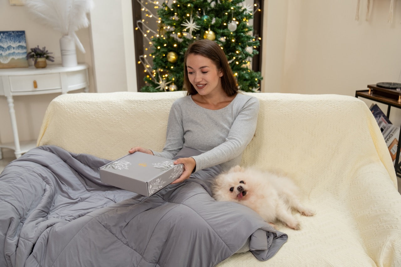 Woman sitting on a couch with a small dog, holding a box, in a cozy living room setting.