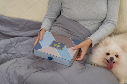 Person holding happy hoos' winter themed notebook set gift box with a dog sitting next to them on a bed