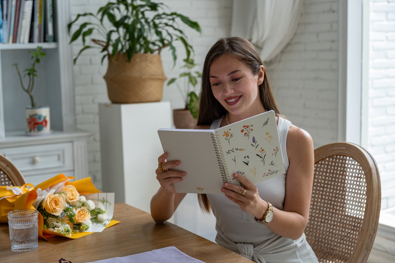 Woman reading a notebook at a table with a cozy indoor setting