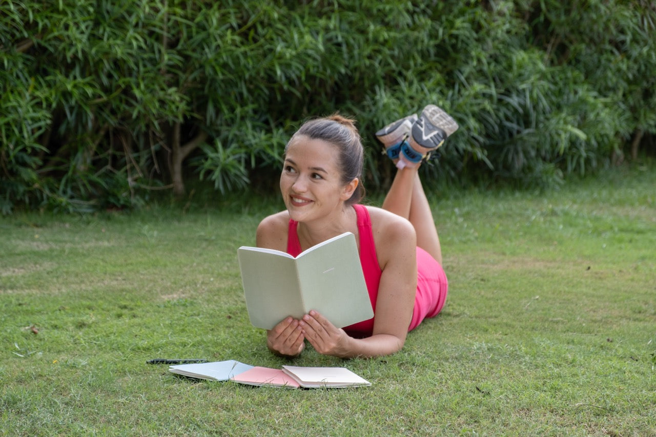 Woman lying on grass holding a notebook while smiling 
