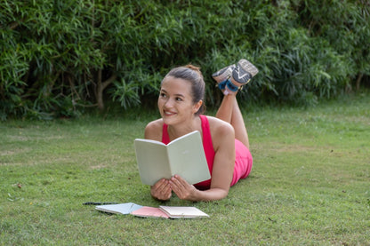 Woman lying on grass holding a notebook while smiling 