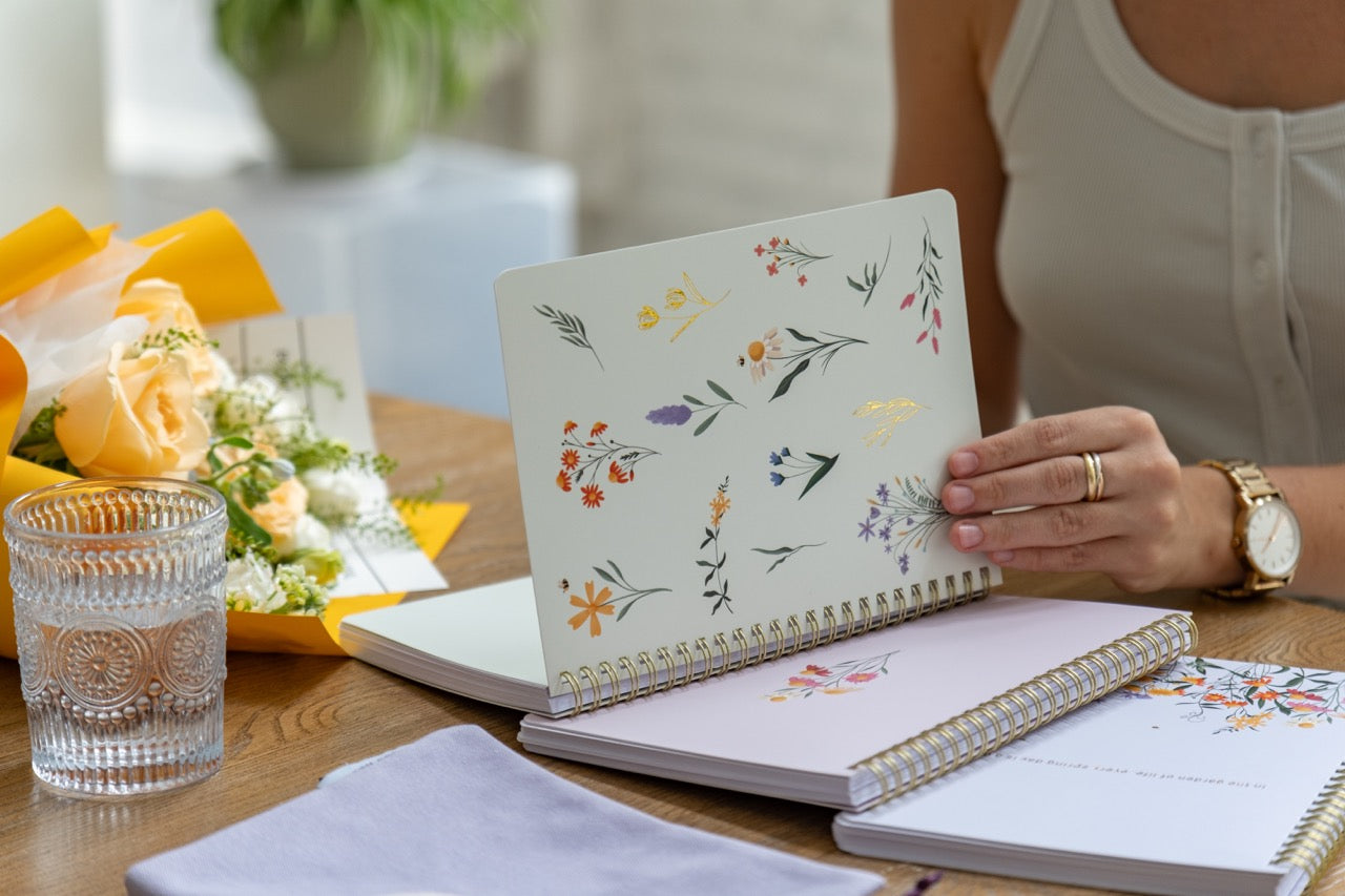 Person holding a floral planner with a glass of water and flowers on a table.
