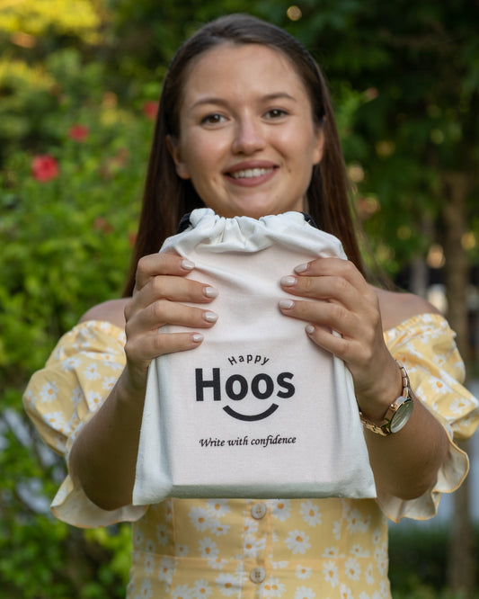 Woman holding a white bag with 'Happy Hoos' text against a blurred green background