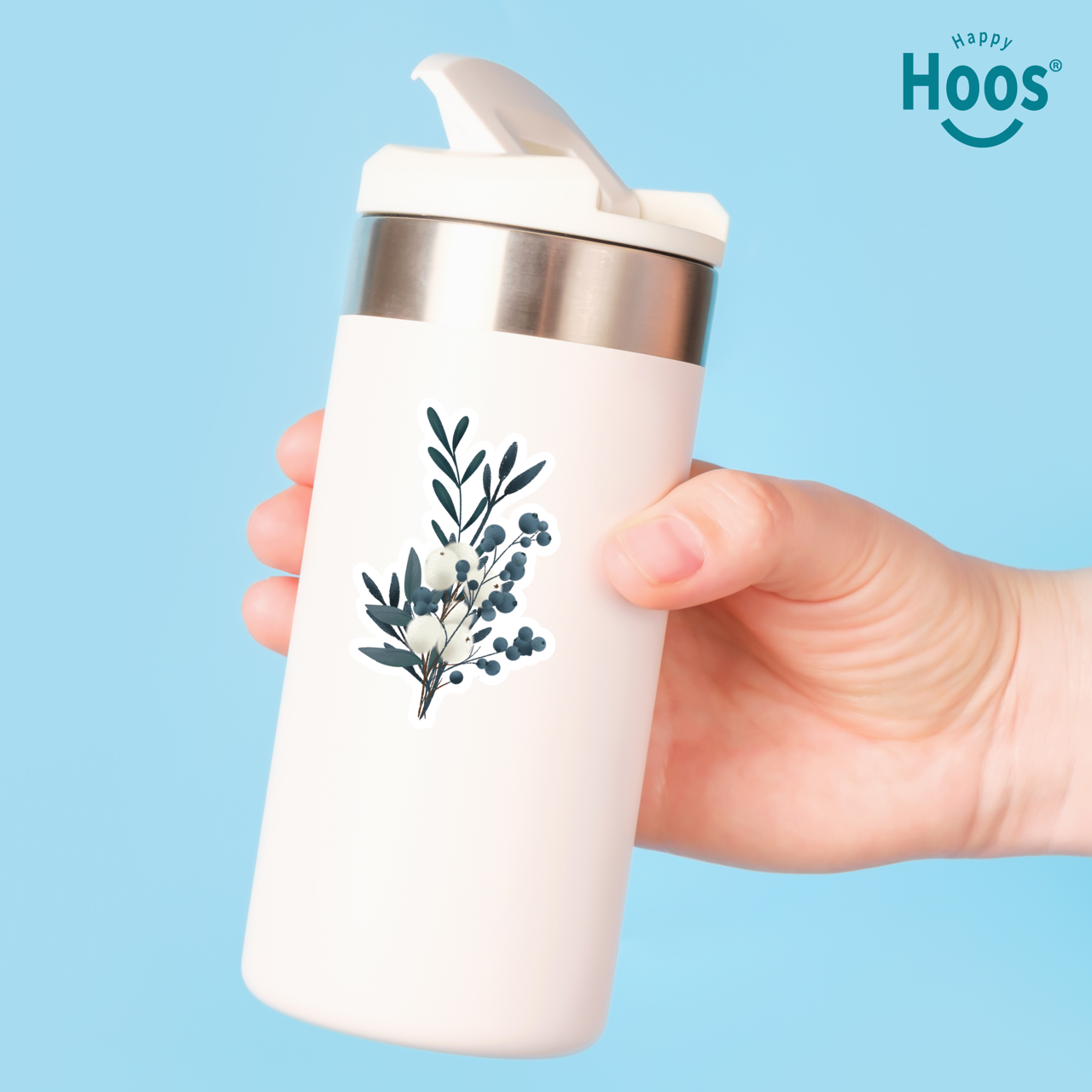 White tumbler with Winter Eucalyptus floral design held by a hand against a blue background, featuring the 'Happy Hoos' brand.