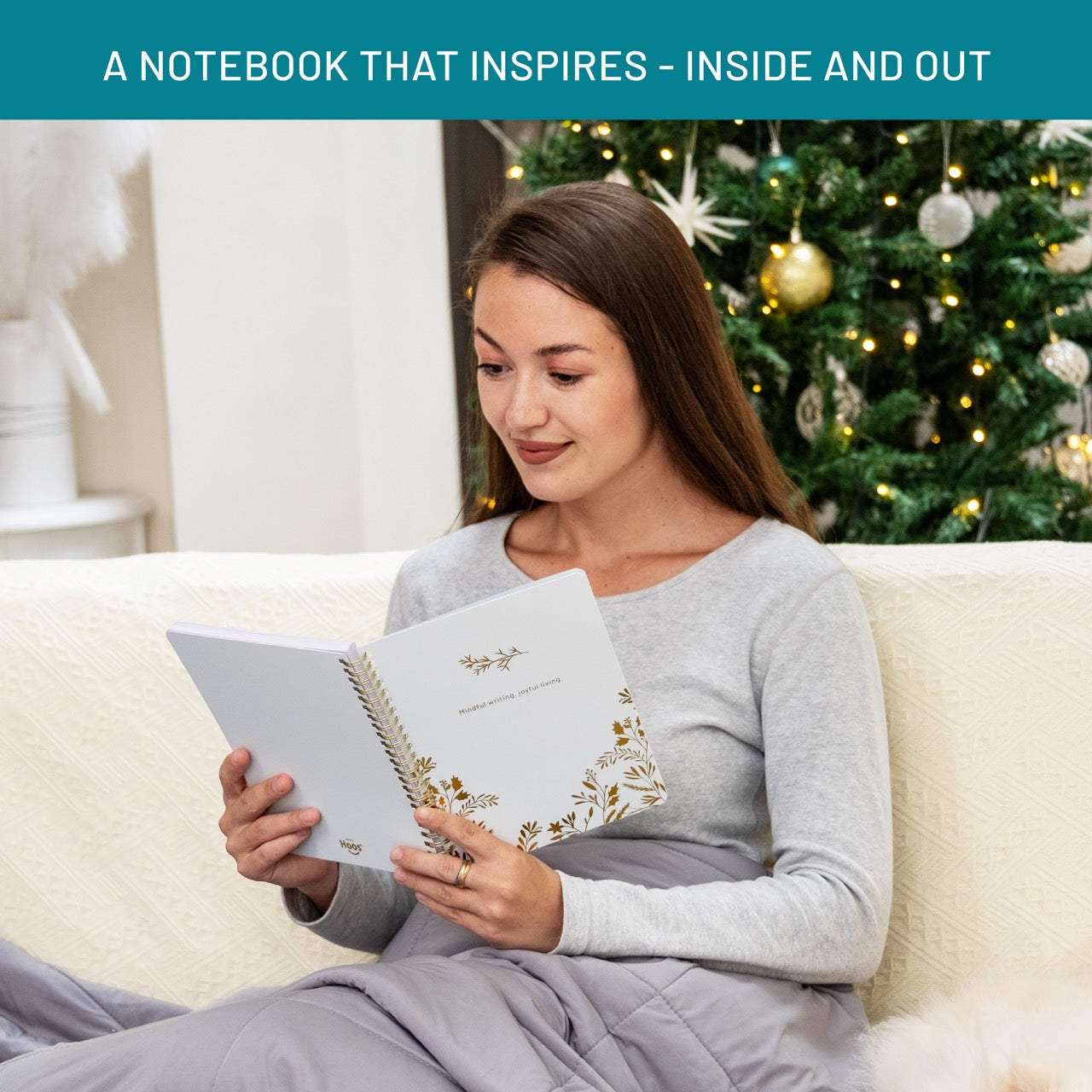 Woman reading a notebook on a couch with a decorated Christmas tree in the background