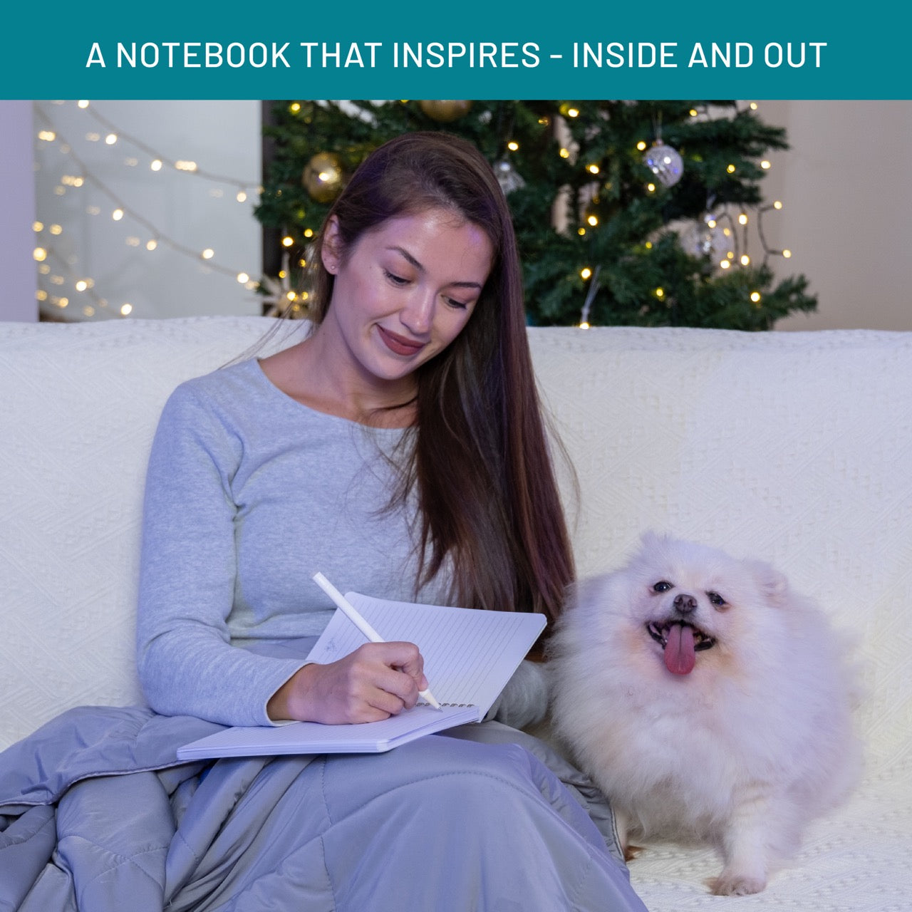 Woman sitting on a couch with a notebook and a dog, surrounded by festive decorations.