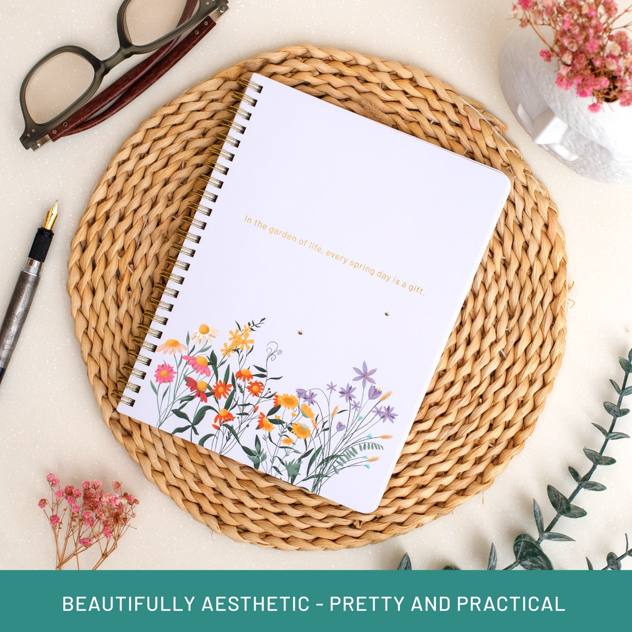 Notebook with floral design on a woven mat with glasses and pen