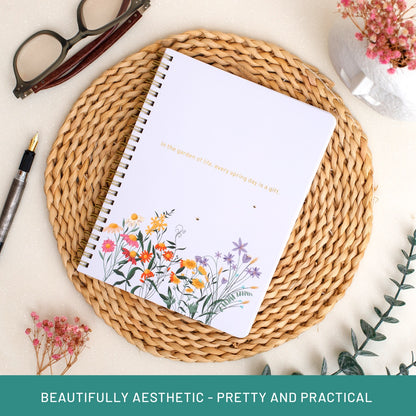 Notebook with floral design on a woven mat with glasses and pen