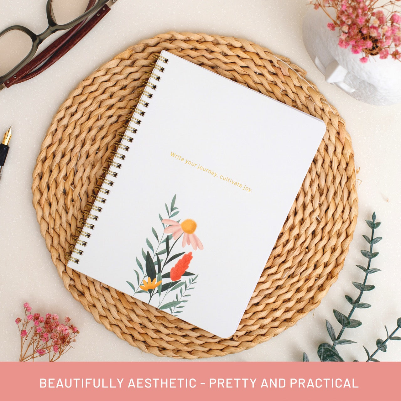 Notebook with floral design on a woven mat with flowers and glasses in the background
