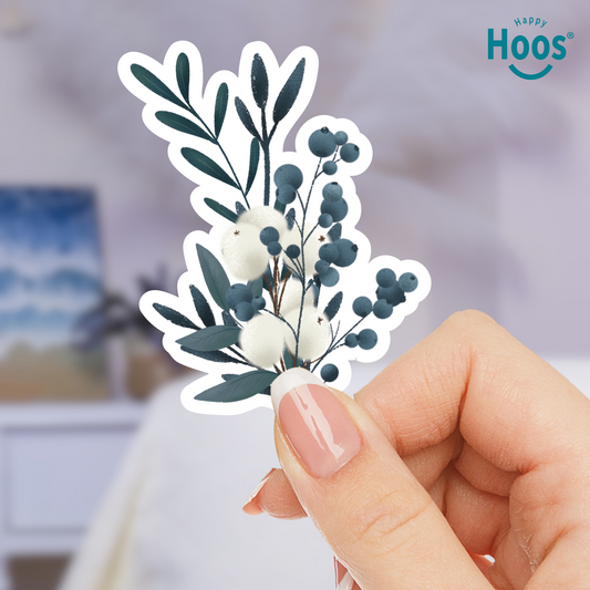 Hand holding a decorative sticker with winter eucalyptus floral design, brand 'Happy Hoos' visible