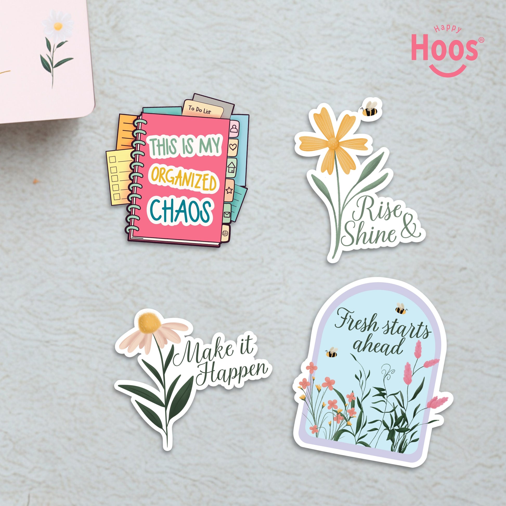 Four motivational stickers on textured surface: 'This is My Organized Chaos' planner, 'Rise Shine &' yellow flower, 'Make it Happen' daisy, and 'Fresh starts ahead' floral arch