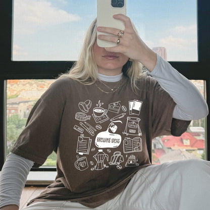 Person wearing a brown t-shirt with white graphics and text, sitting indoors.