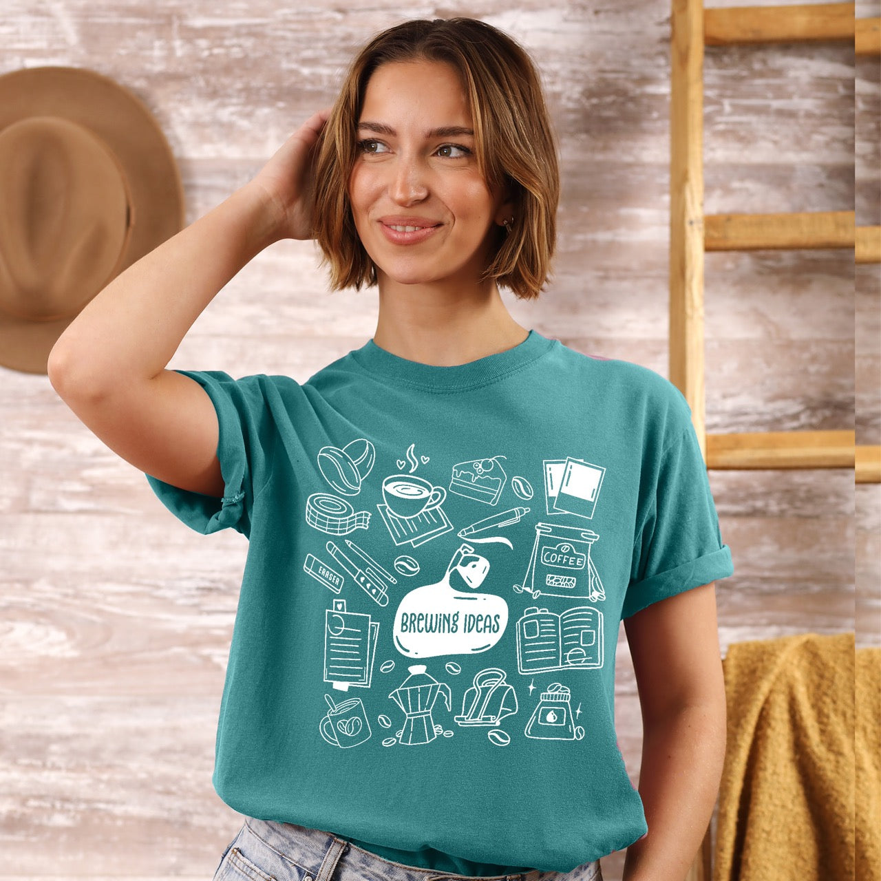 Woman wearing a teal t-shirt with white coffee-themed graphics against a wooden background.