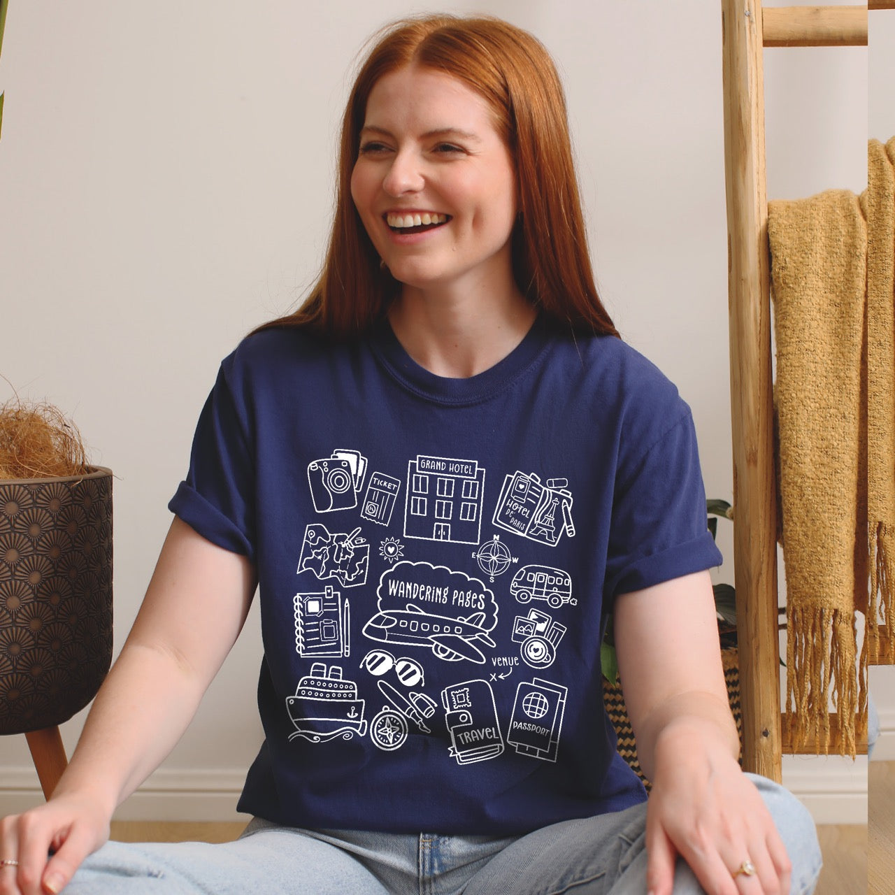 Person wearing a navy blue t-shirt with white graphics  on travel and writing - woman is sitting indoors.