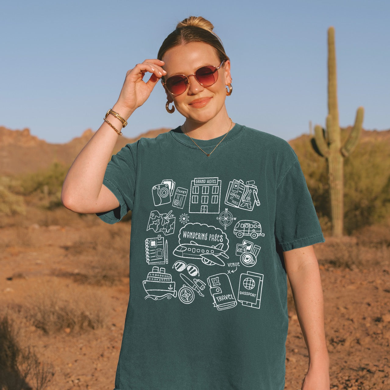 Woman in the dessert wearing Happy Hoos' Travel Doodle shirt which features writing and travel doodles. 