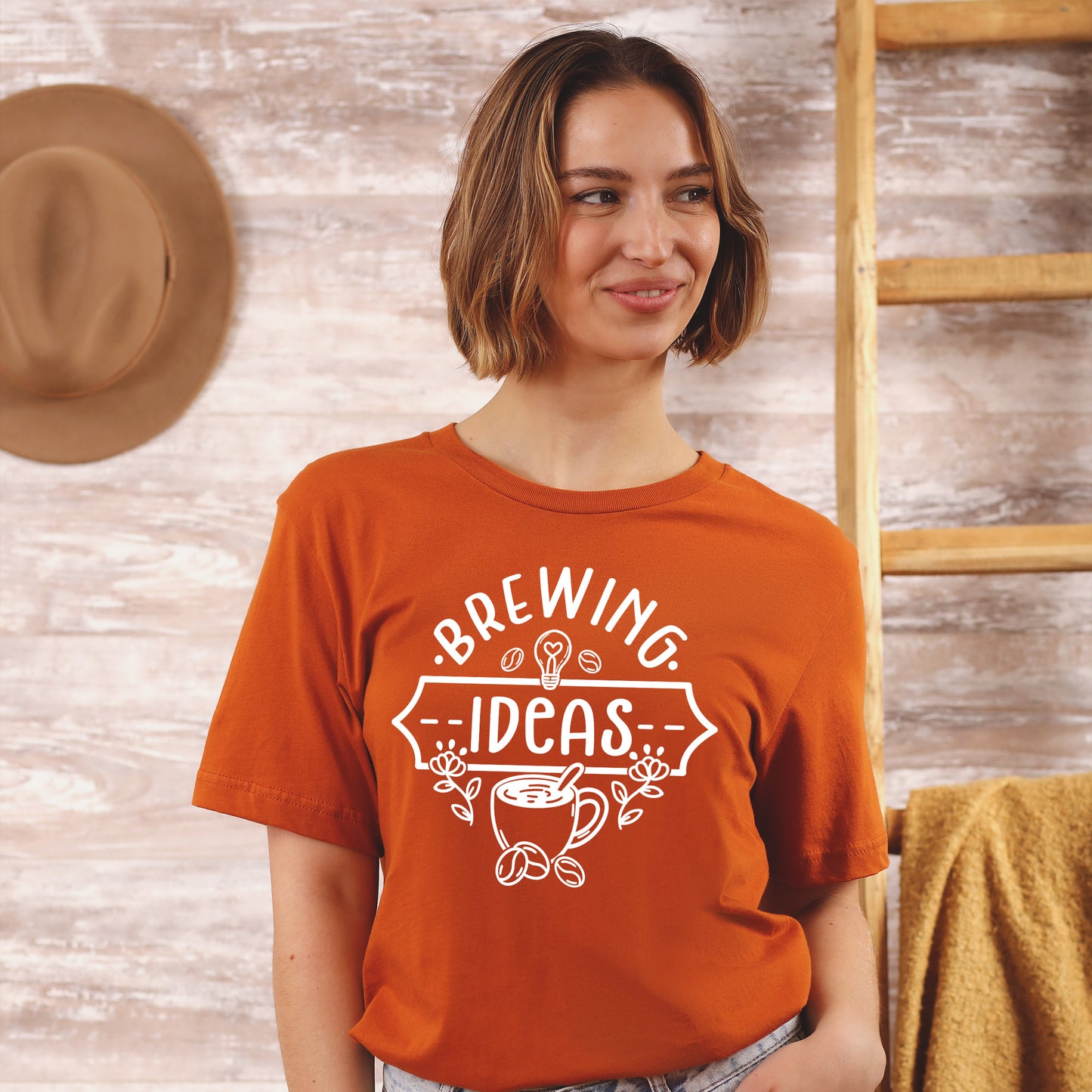 Woman wearing an orange t-shirt with 'Brewing Ideas' design against a wooden background