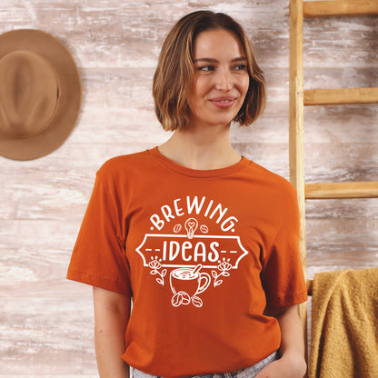 Woman wearing an orange t-shirt with 'Brewing Ideas' design against a wooden background
