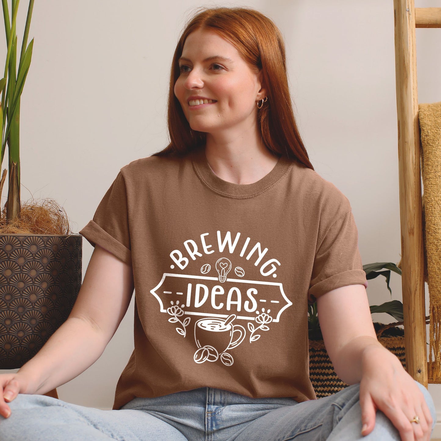 Person wearing a brown t-shirt with 'Brewing Ideas' design, sitting indoors.
