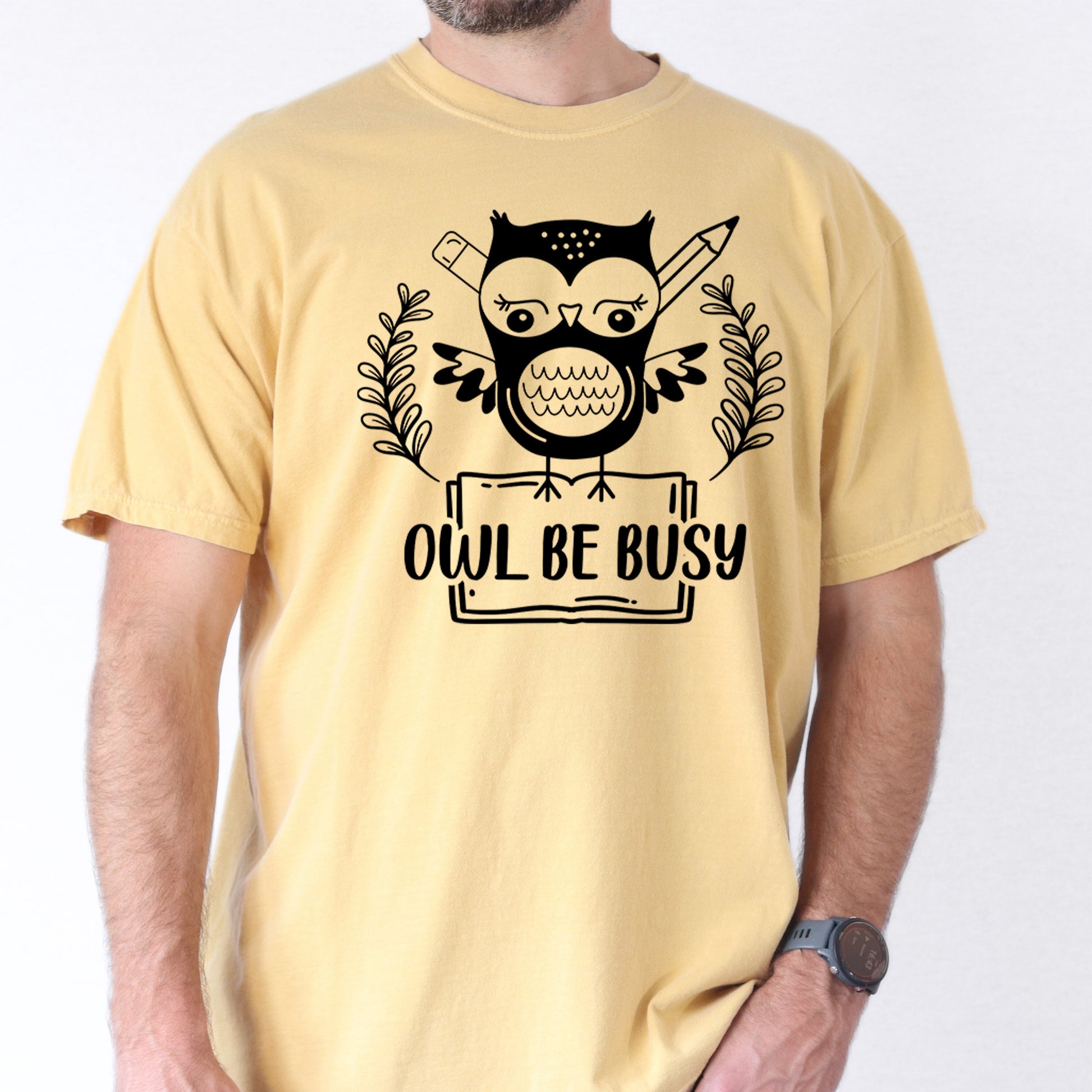 Person wearing butter colored  t-shirt with an owl graphic and 'OWL BE BUSY' text.