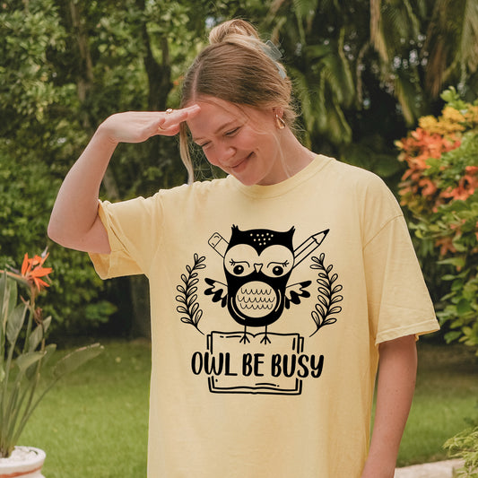 Person wearing butter colored  t-shirt with an owl graphic and 'OWL BE BUSY' text.