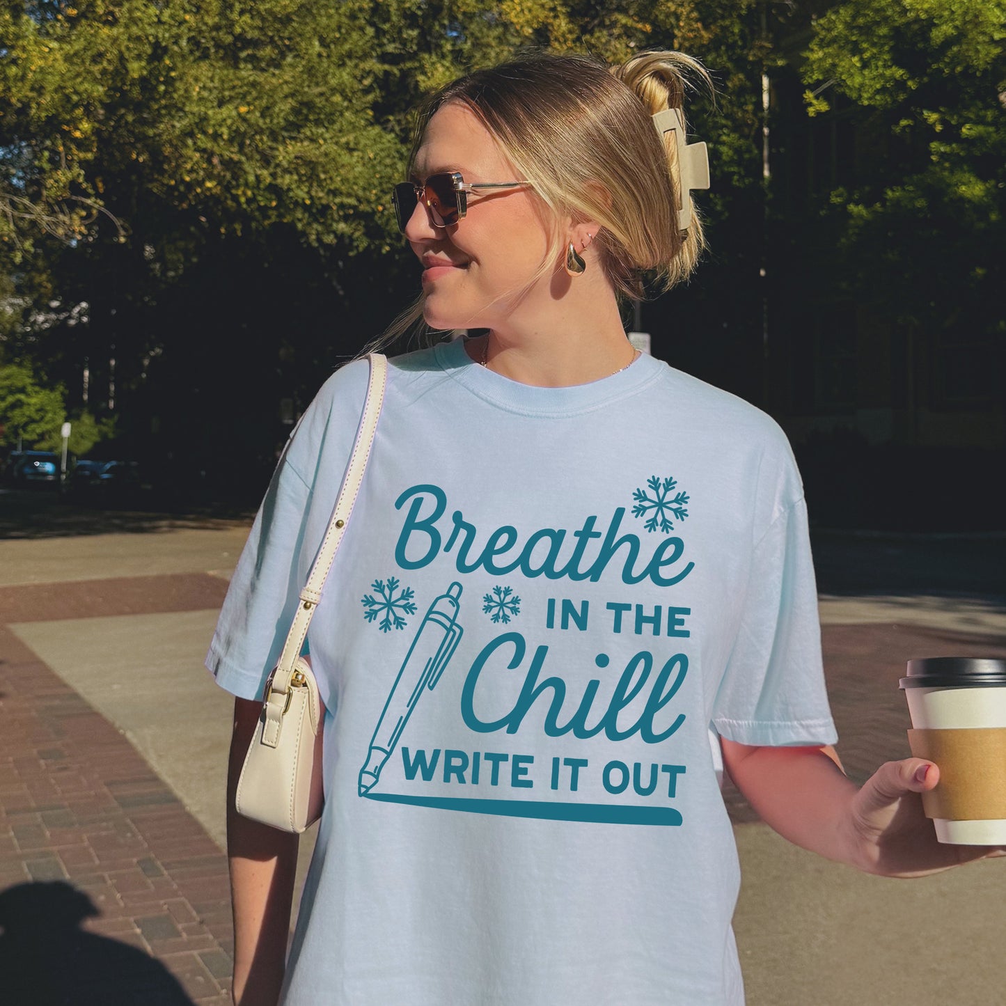 Person wearing a Light blue t-shirt with blue text "Breath in the Chill, Write it out" and graphics on a white background