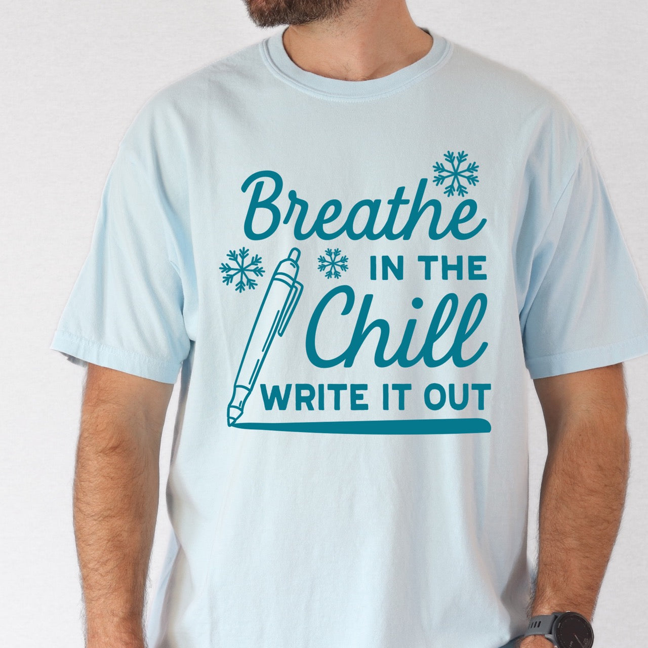 Light blue t-shirt with motivational text "Breath in the Chill, Write it out"  and graphics on a plain background