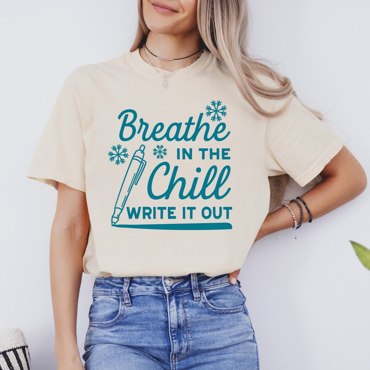 Person wearing a beige t-shirt with blue text "Breath in the Chill, Write it out" and graphics on a white background