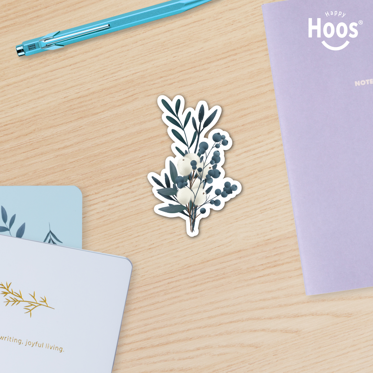 Winter Eucalyptus Floral sticker on a wooden surface with notebooks and a pen.