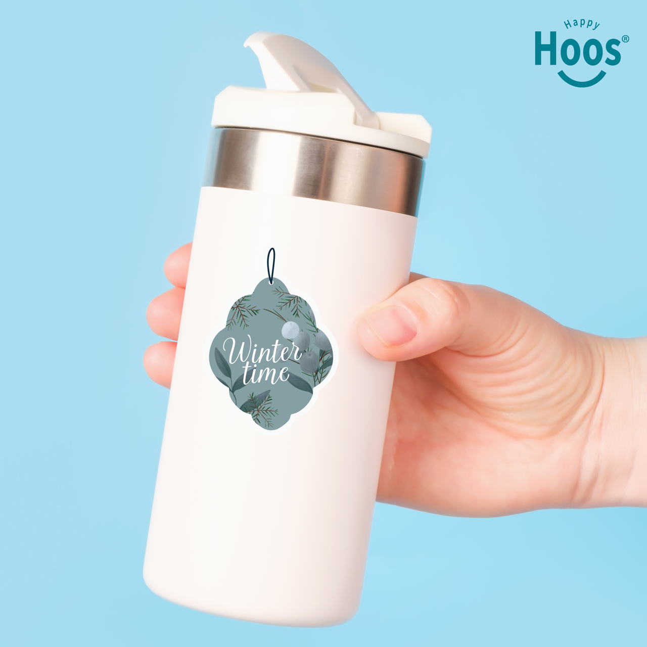 White tumbler with 'Winter time' design sticker held by a hand against a blue background, featuring the 'Happy Hoos' brand.