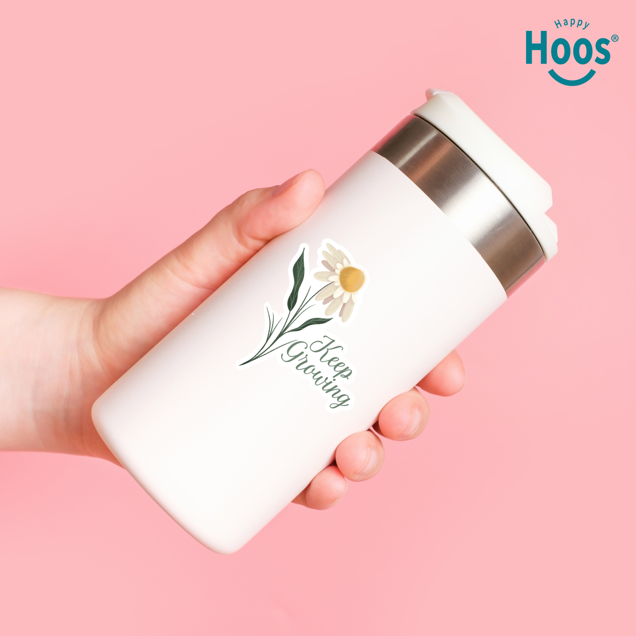 Hand holding a white thermos with floral design and 'Keep Growing' text on a pink background, featuring the 'Happy Hoos' brand.