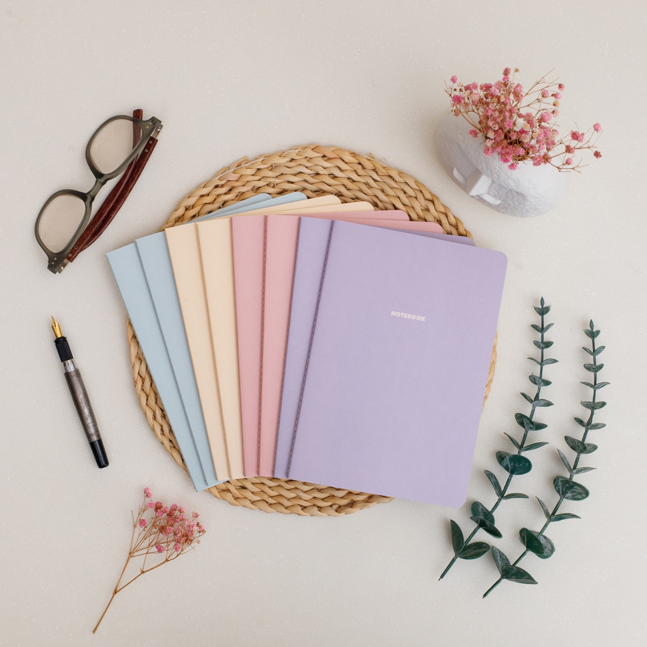 Set of 8 colorful summer inspired notebooks on a woven mat with a pen and small plant on a light background