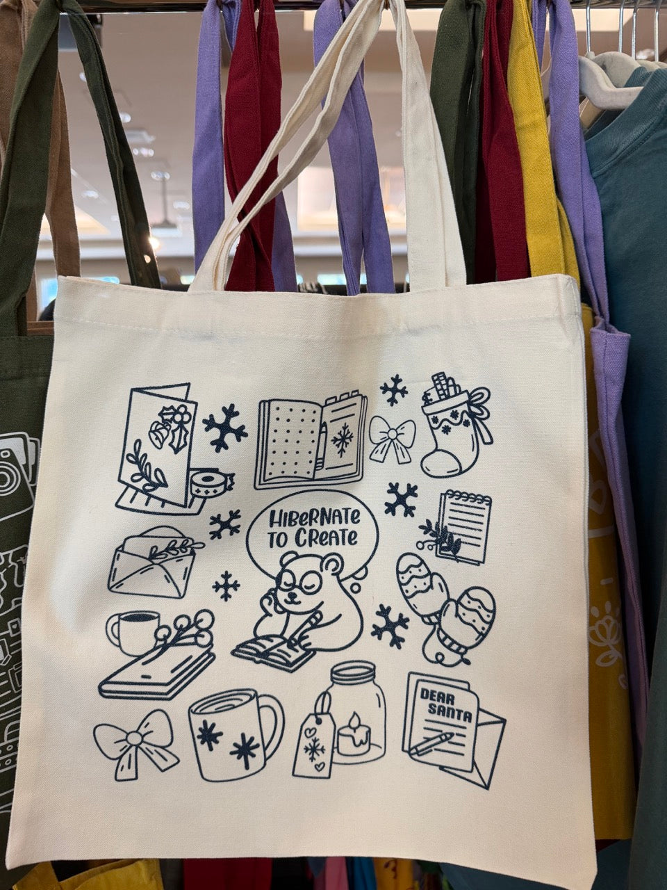 Tote bag with blue illustrations  on writing, journaling and winter hanging on a rack
