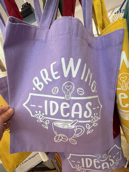 Purple tote bag with 'Brewing Ideas' text held by a hand in a store setting.