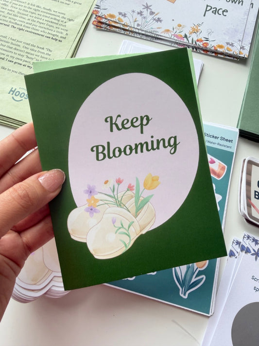 Keep Blooming floral greeting card featuring blooming nursing clogs with spring flowers on a dark green background