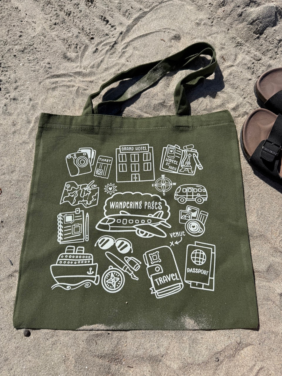 Green tote bag with travel-themed illustrations on a sandy surface - tote bag with theme on journaling and traveling