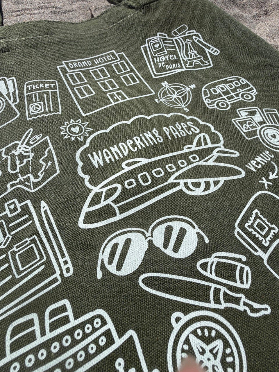 Green fabric with white line art illustrations including a plane, sunglasses, and buildings. theme of wandering pages - journaling and traveling
