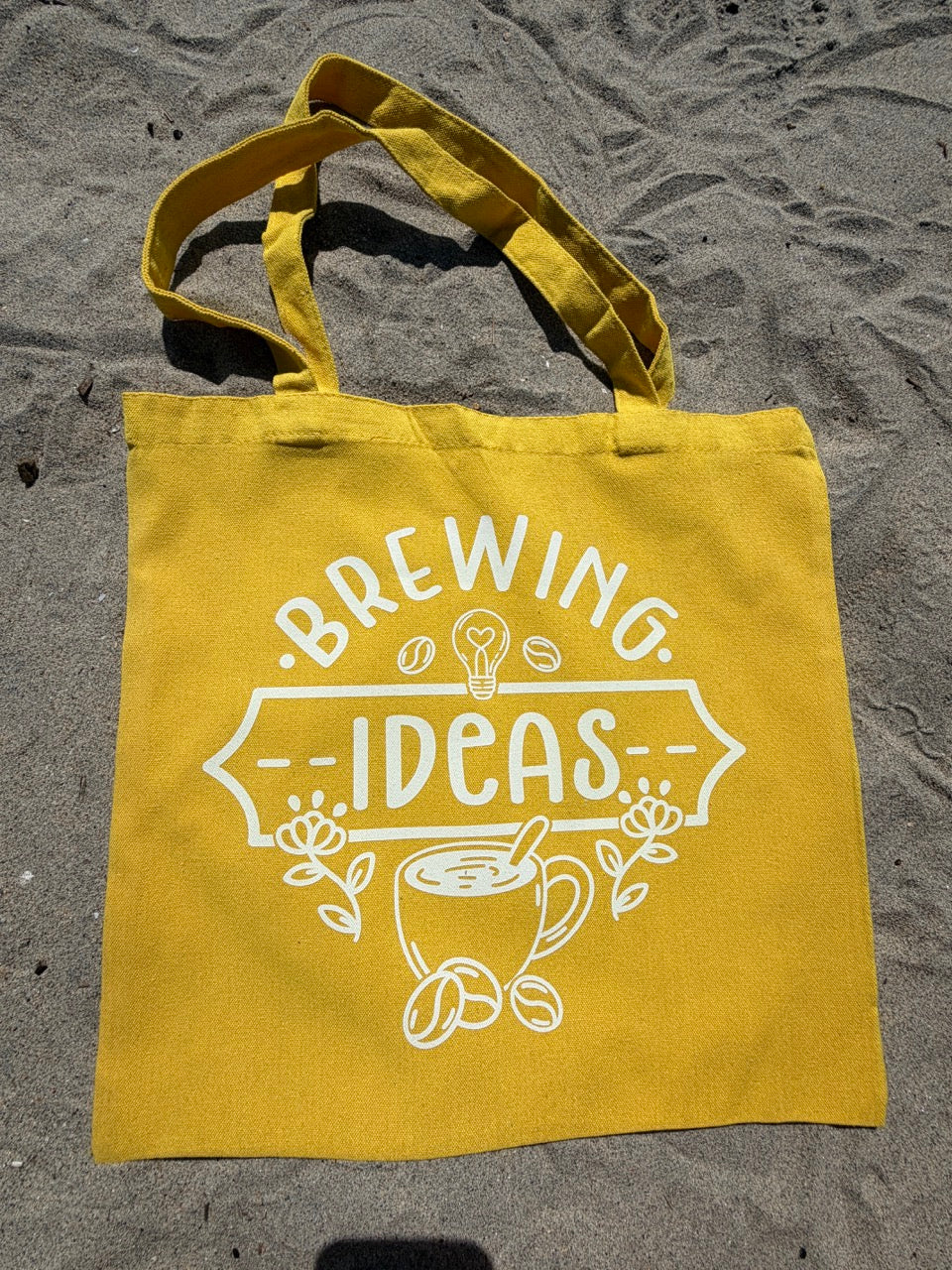 Yellow tote bag with 'Brewing Ideas' text and graphics on a textured surface