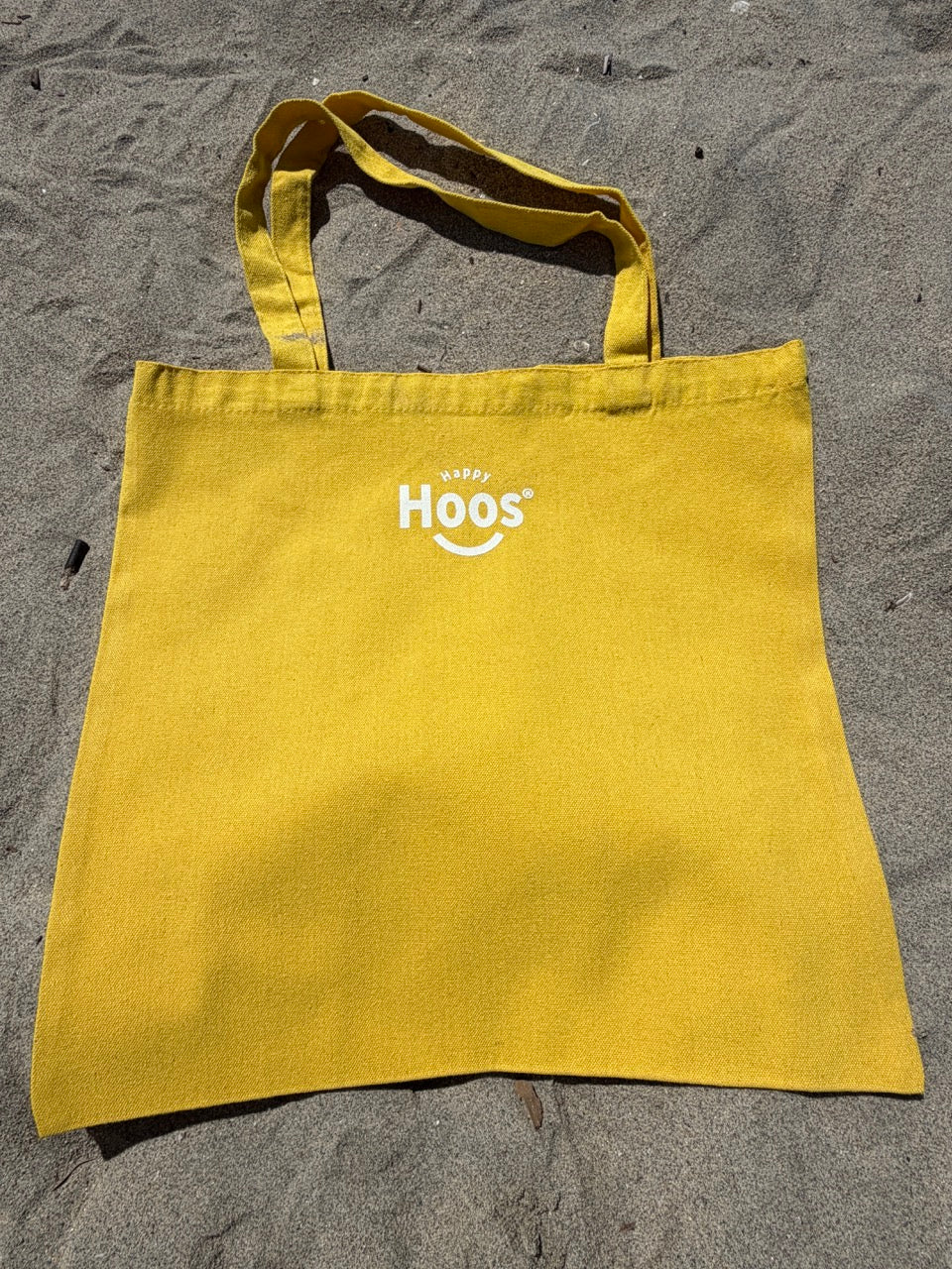 Yellow tote bag with "Happy Hoos' logo on a sandy surface
