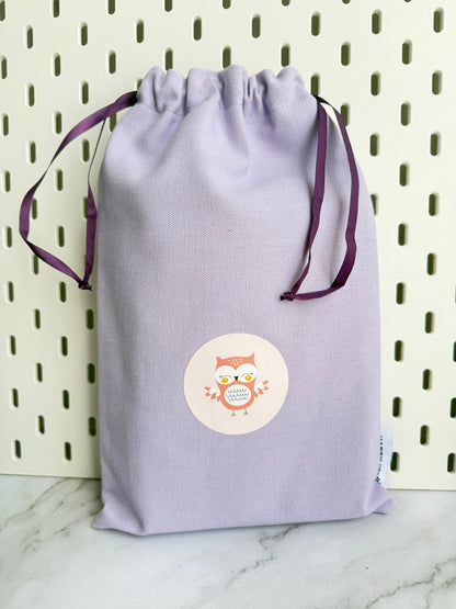Light purple drawstring bag with a circular label featuring an owl design on a white background.