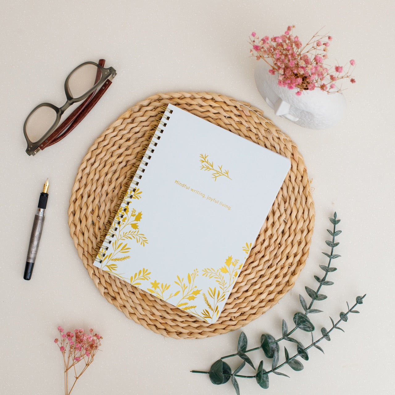 Notebook with floral design on a woven mat with glasses and pen