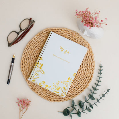 Notebook with floral design on a woven mat with glasses and pen